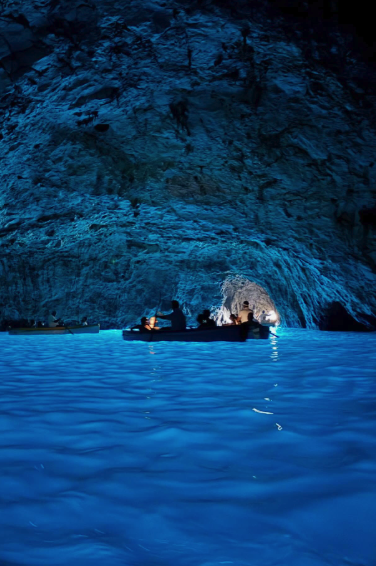Rowboats on the luminous blue water inside the Blue Grotto